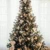 Christmas tree in front of a large window decorated with gold and white ornaments designed by Eleni Decor