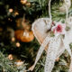 A heart shaped felt ornament decorated with a porcelain rose and lace ribbon is hanging on a Christmas tree