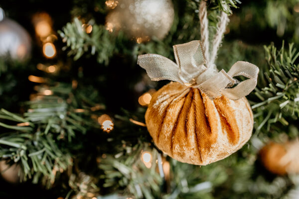 An golden velvet ball with a gold bow hanging on a Christmas tree