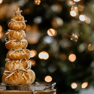 A golden velvet tree with a gold star on top sitting on a real wood base is pictured in front of a Christmas tree