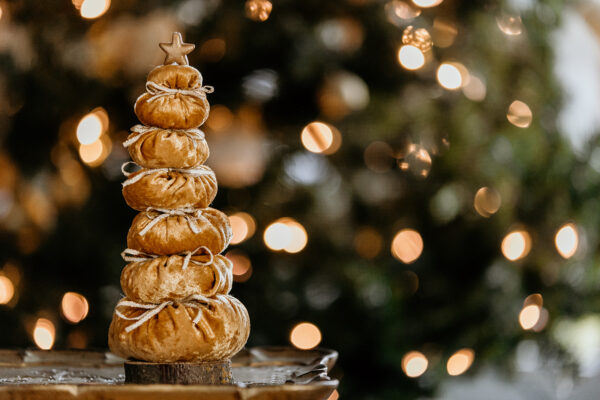 A golden velvet tree with a gold star on top sitting on a real wood base is pictured in front of a Christmas tree