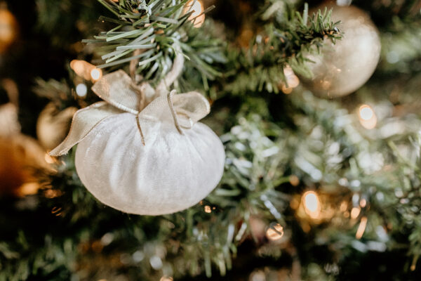 An off white colored velvet ball with a gold bow hanging on a Christmas tree