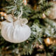 An off white colored velvet ball with a gold bow hanging on a Christmas tree