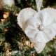 A heart shaped felt ornament decorated with a fabric flower and jeweled center is hanging on a Christmas tree